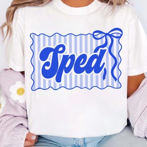 May include: White t-shirt featuring a blue design with the word "Sped" in a bold, cursive font. The design includes a blue striped background and a decorative bow. The shirt is made of a soft material.