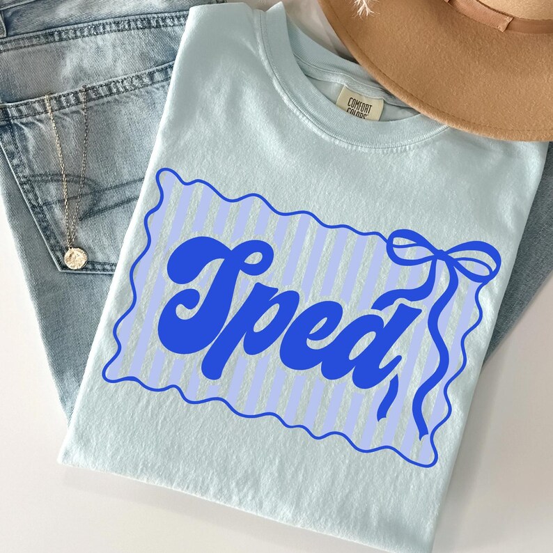 May include: A light blue t-shirt with the word "Spead" in a blue, retro font. The word is inside a blue scalloped border with vertical stripes and a bow. The shirt is folded on top of a pair of blue jeans.