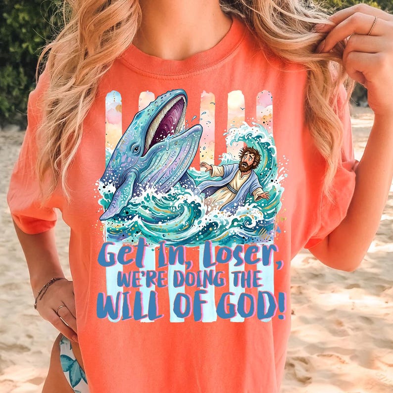 May include: Coral-colored t-shirt featuring a graphic of a whale, a person in water, and the text "Get In, Loser, We're Doing The Will Of God!" The design includes blue, teal, and white colors.