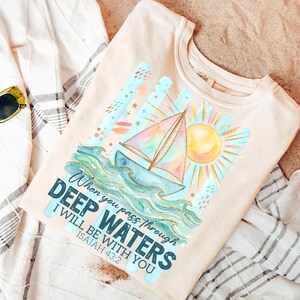 K&ouml;nnte beinhalten: Beiges Sweatshirt mit einem Aquarelldesign eines Segelbootes auf Wellen, einer Sonne und dem Text "When you pass through deep waters, I will be with you, Isaiah 43:2." Das Design enth&auml;lt blaue, t&uuml;rkisfarbene, gelbe und goldene Akzente.