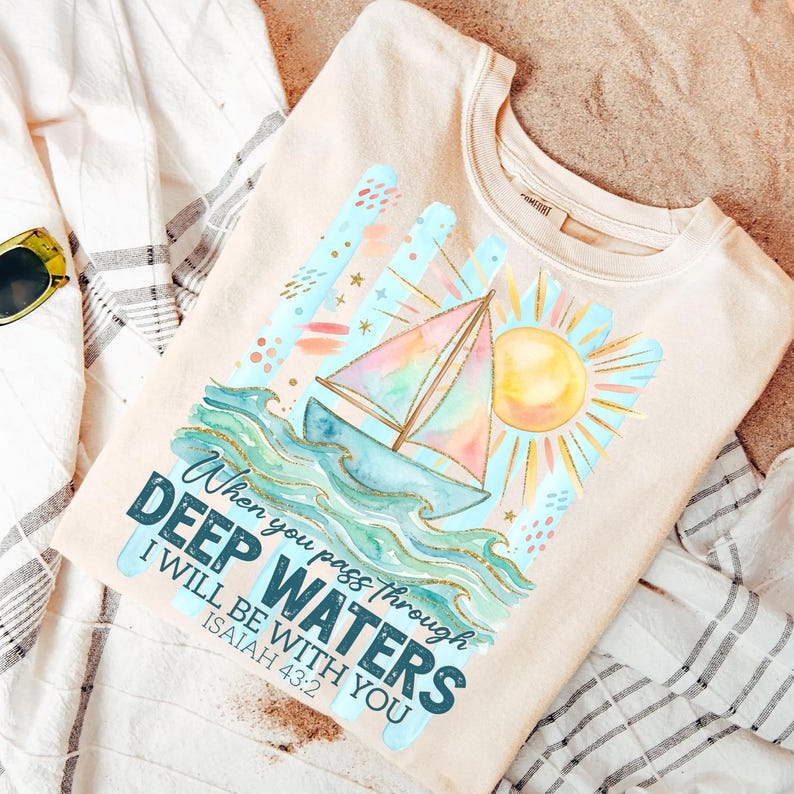 K&ouml;nnte beinhalten: Beiges Sweatshirt mit einem Aquarelldesign eines Segelbootes auf Wellen, einer Sonne und dem Text "When you pass through deep waters, I will be with you, Isaiah 43:2." Das Design enth&auml;lt blaue, t&uuml;rkisfarbene, gelbe und goldene Akzente.