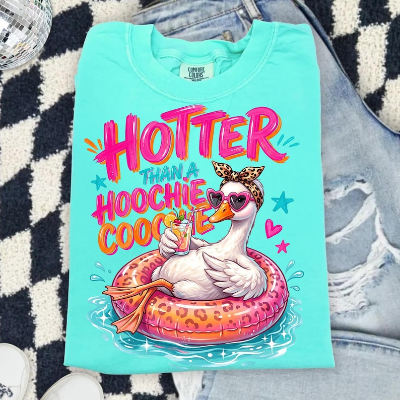 K&ouml;nnte beinhalten: T&uuml;rkisfarbenes T-Shirt mit einer Grafik einer Gans in einem Leoparden-Schwimmring, die eine herzf&ouml;rmige Sonnenbrille und ein Leoparden-Stirnband tr&auml;gt. Der Text lautet "Hotter Than a Hoochie Coochie."