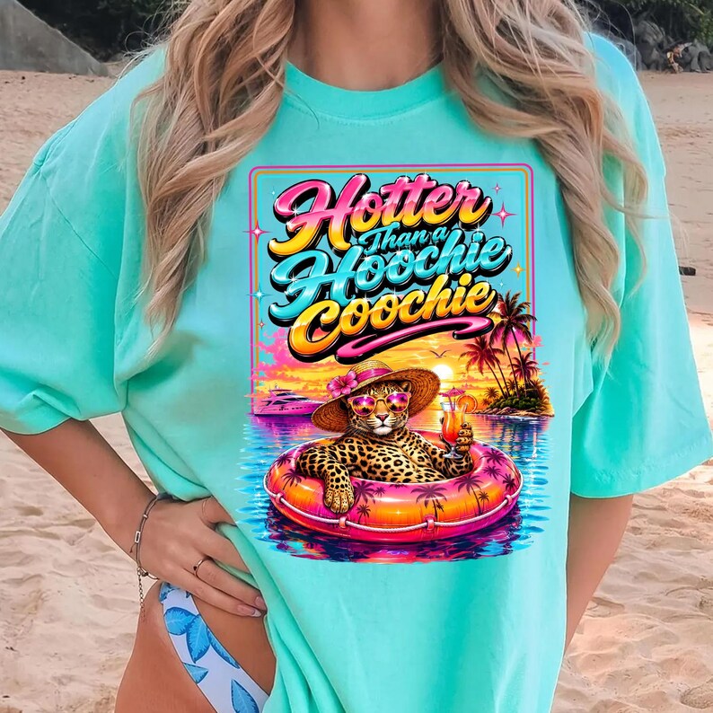 May include: A turquoise t-shirt features a graphic of a leopard wearing sunglasses and a hat, floating in a pool with a tropical sunset backdrop. The text "Hotter Than a Hoochie Coochie" is displayed above the leopard.