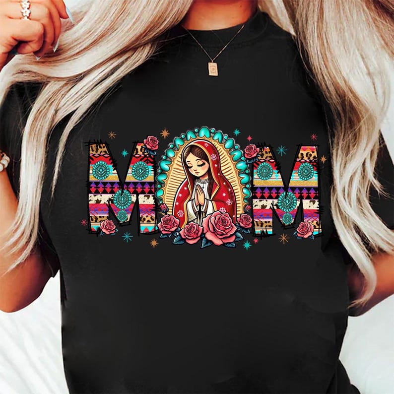 May include: Black t-shirt featuring the word "MOM" in a colorful, patterned design. The "O" is a depiction of a praying figure with a halo, surrounded by pink roses. The shirt has a crew neck.