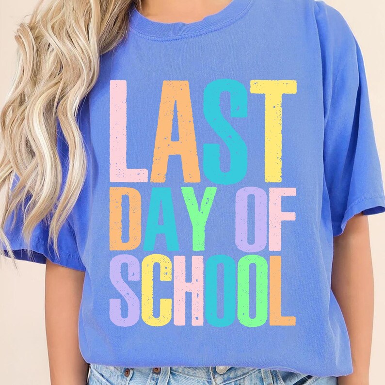 May include: A blue t-shirt with the words "LAST DAY OF SCHOOL" in colorful block letters. The text is in various pastel colors, including pink, orange, yellow, green, and purple. The shirt has short sleeves and a crew neck.