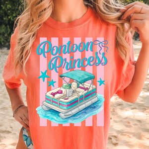 May include: Coral-colored t-shirt with the text "Pontoon Princess" in turquoise script. The design includes a cartoon pontoon boat with a turquoise canopy, blue water, and turquoise stars. The shirt has a striped background.