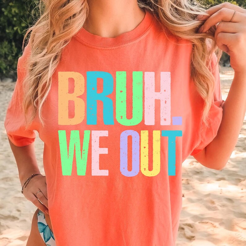May include: Coral-colored t-shirt with the text "BRUH. WE OUT" in colorful block letters. The shirt has a crew neck and short sleeves. The image shows the shirt being worn.