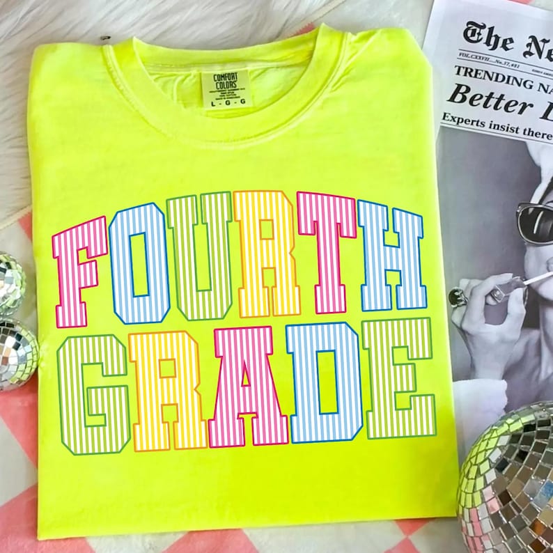 May include: A neon yellow short-sleeve t-shirt featuring the text "FOURTH GRADE" in a collegiate font. The letters are filled with vertical stripes in alternating colors of pink, blue, yellow, and green. A Comfort Colors brand tag is at the neck.