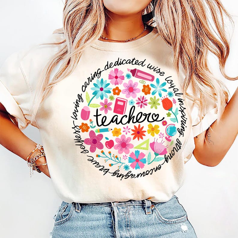 May include: A white t-shirt with a circle design featuring colorful flowers, school supplies, and the word "teacher" in the center. The circle is surrounded by the words "strong, brave, kind, loving, caring, dedicated, wise, loyal, inspiring".
