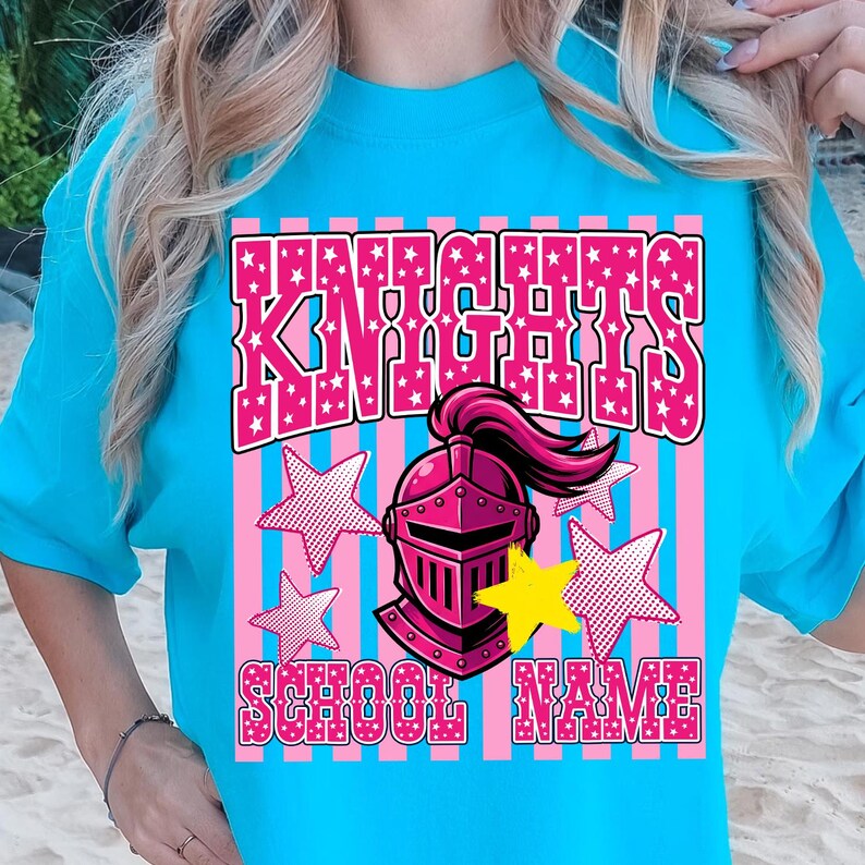 May include: A turquoise t-shirt with a pink and white design. The design features the word "KNIGHTS" in a pink, star-filled font, a pink knight's helmet, and the words "SCHOOL NAME". Pink and white stars are also included.