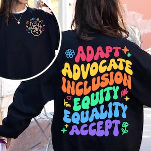 May include: Black sweatshirt with a rainbow-colored graphic on the back that says "ADAPT + ADVOCATE INCLUSION EQUITY EQUALITY ACCEPT". The graphic is in a retro font style with flowers and other small designs.