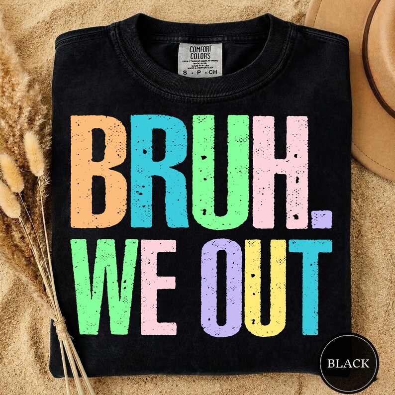 May include: Black t-shirt with the phrase "BRUH. WE OUT" in large, colorful, block letters. The text is in shades of orange, blue, green, pink, purple, and yellow. The shirt has a Comfort Colors tag and a black circle that says "BLACK".