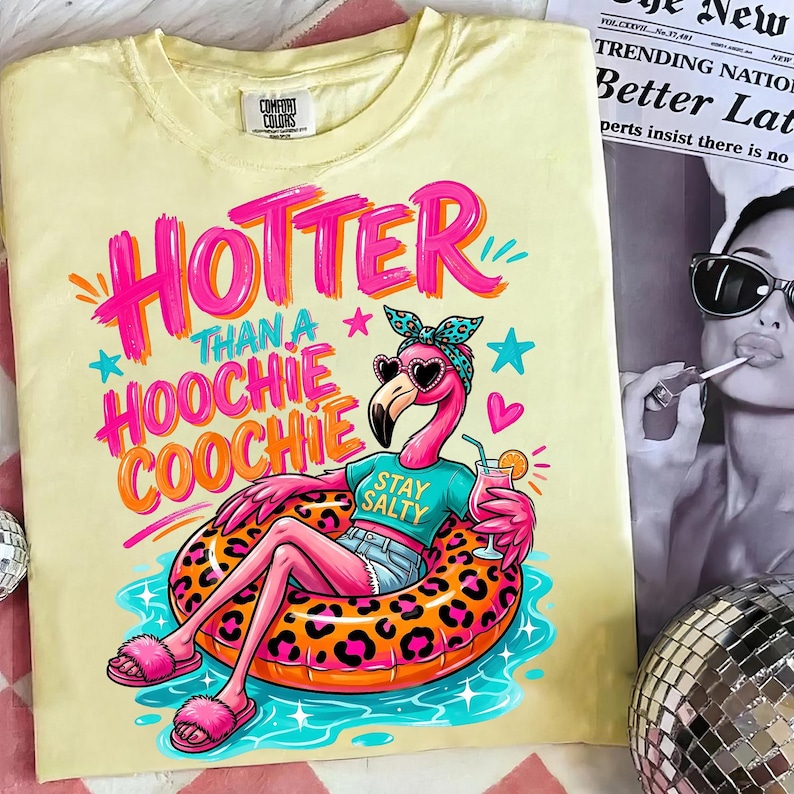 K&ouml;nnte beinhalten: Gelbes Comfort Colors T-Shirt mit einem Flamingo-Motiv, das eine Sonnenbrille in Herzform und ein Stirnband tr&auml;gt und auf einem Leopardenmuster-Schwimmring liegt. Der Text lautet "HOTTER THAN A HOOCHIE COOCHIE" und "STAY SALTY".