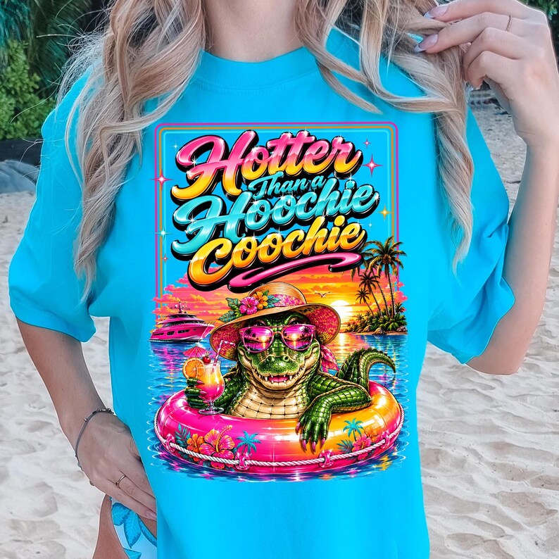 May include: A turquoise t-shirt features a colorful graphic of an alligator in sunglasses and a hat, floating in a pool with a cocktail. The text reads "Hotter Than a Hoochie Coochie" in a retro font, with a tropical sunset background.