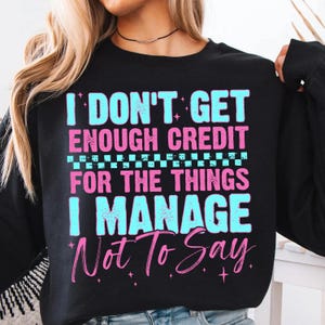 May include: Black sweatshirt with the text "I DON'T GET ENOUGH CREDIT FOR THE THINGS I MANAGE Not To Say" in light blue and pink lettering. The sweatshirt has a crew neck and long sleeves.
