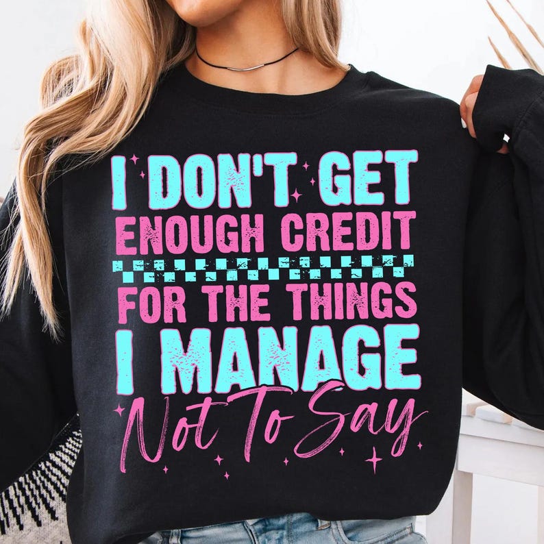 May include: Black sweatshirt with the text "I DON'T GET ENOUGH CREDIT FOR THE THINGS I MANAGE Not To Say" in light blue and pink lettering. The sweatshirt has a crew neck and long sleeves.