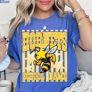 May include: Blue t-shirt with a yellow and white graphic. The graphic features the word "HORNETS" in a star-filled font, a cartoon bee, and the words "SCHOOL NAME". The shirt is a comfortable, casual style.