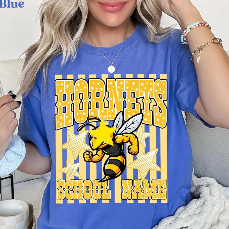 May include: Blue t-shirt with a yellow and white graphic. The graphic features the word "HORNETS" in a star-filled font, a cartoon bee, and the words "SCHOOL NAME". The shirt is a comfortable, casual style.