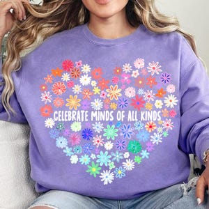 May include: Purple sweatshirt with a heart-shaped design made of colorful flowers. The text "Celebrate Minds of All Kinds" is printed inside the heart.