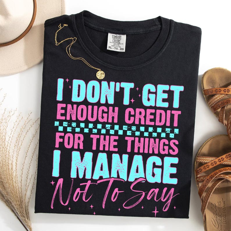 May include: Black Comfort Colors t-shirt with the text "I DON'T GET ENOUGH CREDIT FOR THE THINGS I MANAGE Not To Say" in blue and pink. A gold necklace and brown sandals are also visible.