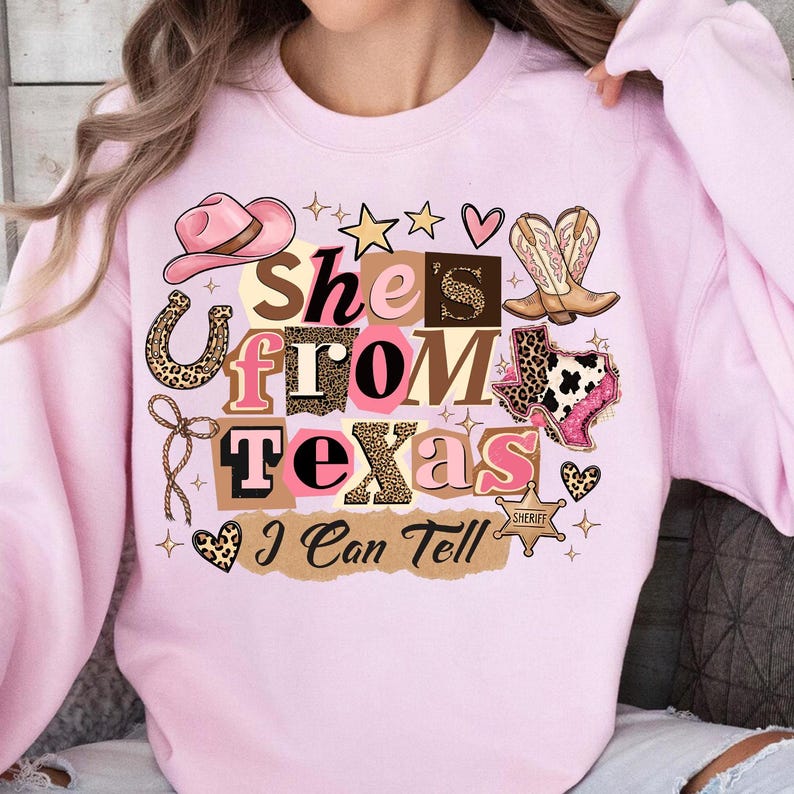 May include: A light pink sweatshirt with a graphic that reads "She's From Texas I Can Tell." The design includes a pink cowboy hat, boots, a horseshoe, and the state of Texas.