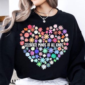 May include: Black sweatshirt with a rainbow heart made of flowers and the text "Celebrate Minds of All Kinds".