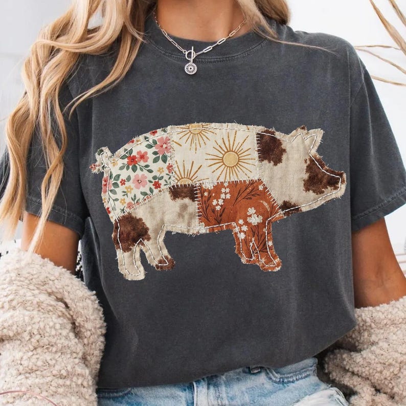 May include: Dark gray t-shirt featuring a patchwork pig design. The pig is composed of various fabric patterns, including floral, sunburst, and cowhide prints. The shirt has short sleeves and a relaxed fit, suitable for casual wear.