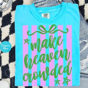 May include: Lagoon blue t-shirt with the text "make heaven crowded" in green script. The design features pink vertical stripes and green stars and a bow. The shirt is folded.