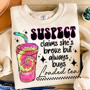 Puede incluir: Una sudadera blanca con un diseño gráfico de un té helado tie-dye rosa y azul con una pajita y el texto "SUSPECT claims she's broke but always buys loaded tea".
