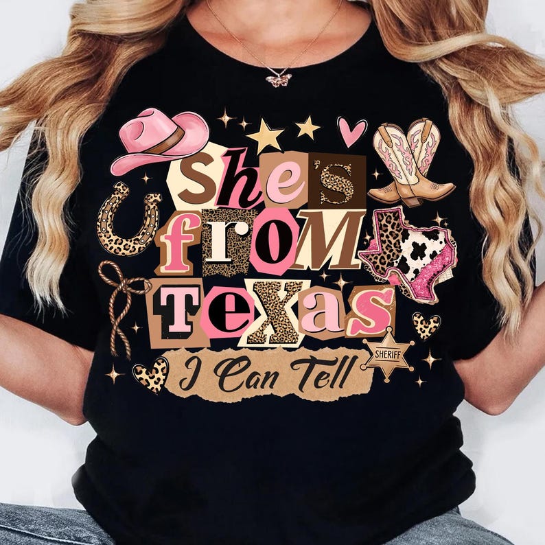 May include: Black t-shirt with a graphic design that reads "She's From Texas I Can Tell." The design includes a pink cowboy hat, boots, a horseshoe, and the outline of the state of Texas.