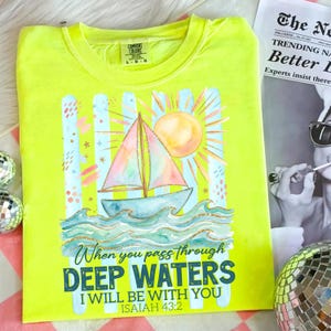 K&ouml;nnte beinhalten: Neongelbes T-Shirt mit einem Aquarelldesign eines Segelbootes auf Wellen, einer Sonne und dem Text "When you pass through deep waters I will be with you Isaiah 43:2". Das Shirt ist von der Marke Comfort Colors.