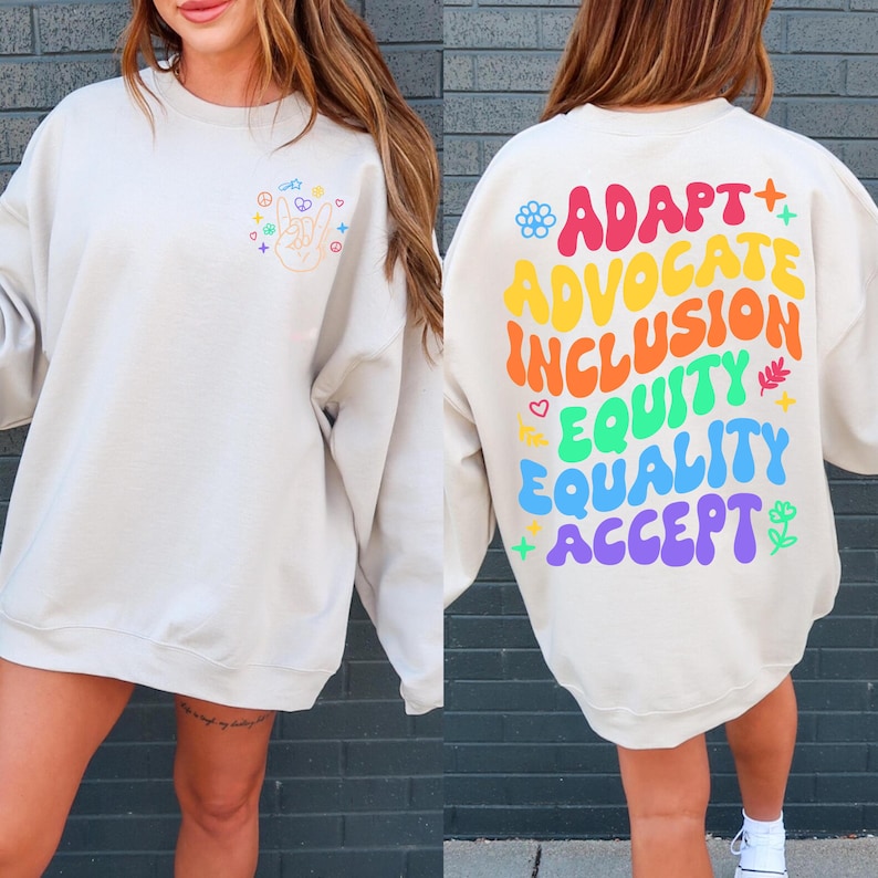 May include: A beige sweatshirt with a peace sign and rainbow colors on the front and the words "Adapt, Advocate, Inclusion, Equity, Equality, Accept" in rainbow colors on the back.