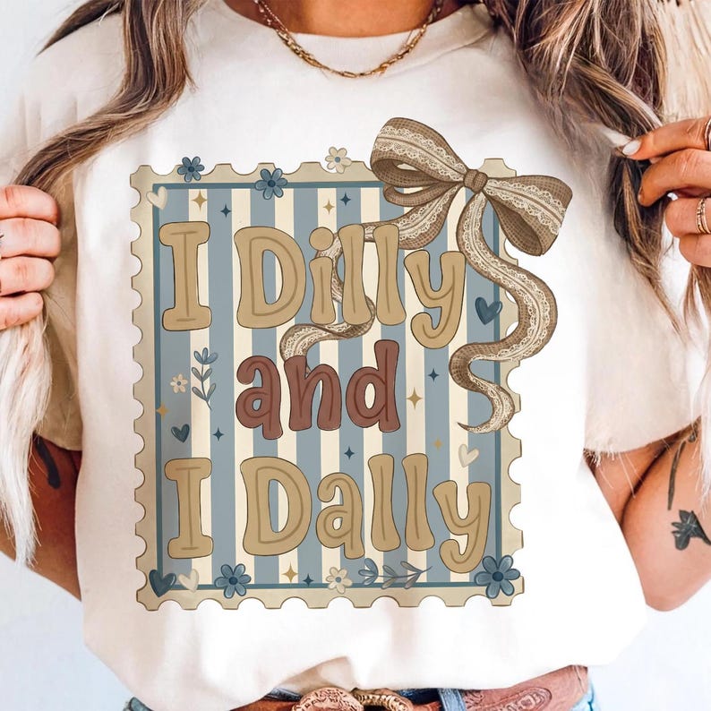 May include: Cream-colored t-shirt featuring the phrase "I Dilly and I Dally" in a vintage-style design. The text is set within a blue and white striped frame, adorned with floral and bow accents. The bow has a lace trim.