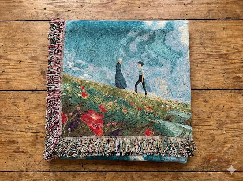 May include: A woven throw blanket featuring a scenic illustration of two figures on a grassy hill with red flowers, under a cloudy sky. The blanket has a fringed edge with shades of red, green, and blue.