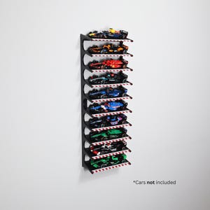 Op de afbeelding: Een zwart aan de muur gemonteerd displayrek met meerdere niveaus, elk met een miniatuur raceauto. De plank heeft een rood-wit gestreepte rand. De tekst "*Cars not included" staat rechtsonder.