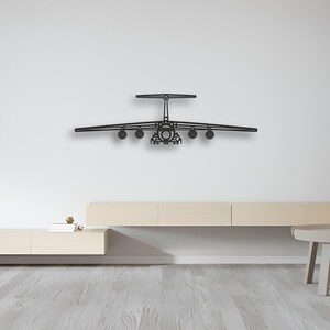 May include: A black metal airplane wall art piece. The airplane has a detailed design with wings, engines, and a tail. The artwork is mounted on a white wall above a light-colored wooden cabinet. The piece adds a modern touch to the room.