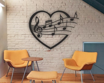 May include: Black metal wall art in the shape of a heart with musical notes and a treble clef inside. The art is hanging on a white brick wall above two yellow chairs and a small yellow ottoman.