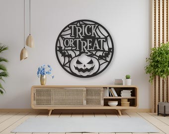 Puede incluir: Arte de pared de Halloween de metal negro con las palabras "Trick or Treat" en un diseño de telaraña. Una cara de calabaza tallada está centrada debajo del texto, con murciélagos a cada lado. La decoración circular está montada en una pared blanca.