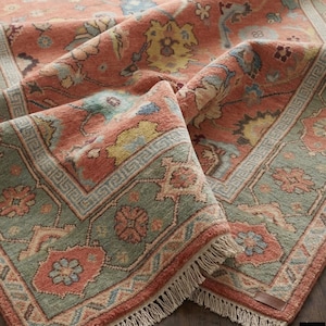 Peut inclure: Gros plan sur un tapis plié et orné. Le tapis présente un motif floral complexe dans les tons corail, jaune, bleu et vert. La bordure est verte contrastante avec des motifs géométriques. Le tapis a une bordure à franges.
