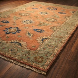 May include: A rectangular area rug in shades of orange and green, featuring a floral design. The rug has a detailed border and fringed edges. It is displayed on a dark wooden floor.