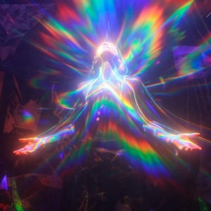 May include: A figure with arms outstretched, illuminated by a vibrant, multi-coloured prismatic light effect that radiates outward from the centre, creating a spectrum of rainbow hues against a dark, indistinct background with subtle textures.
