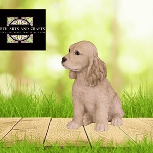 May include: A light tan dog figurine with long, wavy ears and a textured coat, sitting in a seated position. A black square logo in the upper left corner displays the text NORTH ARTS AND CRAFTS INSPIRED BY THE NORTH, CRAFTED WITH CARE.