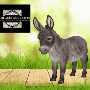 May include: A gray donkey figurine stands on a wooden surface with green grass in the foreground. The donkey has large ears and a detailed coat. A logo for North Arts and Crafts is in the upper left corner.
