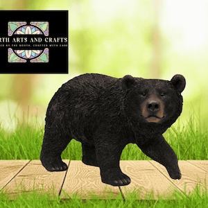 May include: A black bear figurine walking on a wooden surface, with a green grassy background. The bear has a detailed fur texture and a realistic appearance. The image includes the text "NORTH ARTS AND CRAFTS" in a black box.
