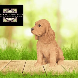 May include: A tan-coloured puppy figurine with long, floppy ears and a textured coat, sitting in a seated position. A black square logo in the upper left corner displays the text NORTH ARTS AND CRAFTS INSPIRED BY THE NORTH CRAFTED WITH CARE.