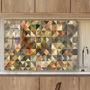 Puede incluir: Un protector contra salpicaduras de cocina con un patrón geométrico de triángulos en tonos marrón, dorado, verde y gris. El protector contra salpicaduras está instalado sobre una encimera y una estufa. La cocina tiene armarios de madera y una mesa redonda.