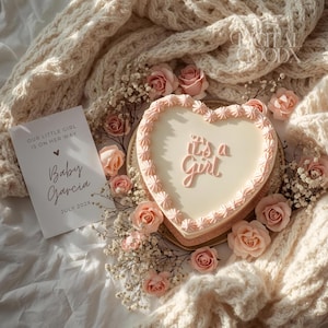 May include: A heart-shaped cake with pink frosting and the words "it's a Girl". The cake is surrounded by pink roses and a card that reads "Our little girl is on her way" and "Baby Garcia July 202X".