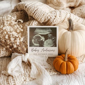K&ouml;nnte beinhalten: Eine Schwangerschaftsank&uuml;ndigung mit einem Ultraschallbild und dem Text "Baby Andersons DUE OCTOBER 202X". Die Szene umfasst einen wei&szlig;en K&uuml;rbis, einen orangefarbenen K&uuml;rbis und einen Strau&szlig; Trockenblumen, alles auf einer cremefarbenen Strickdecke.