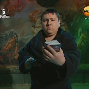 May include: A person in a dark robe holding a deck of cards. The background features a mural with figures and a green and orange logo. The image has a vintage aesthetic, suggesting a theme of fortune telling or mysticism.