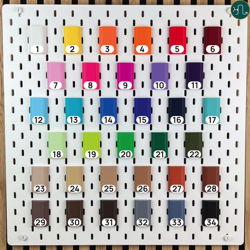 May include: A white rectangular pegboard featuring thirty-four small, rectangular, solid-colored attachments arranged in six rows. Each attachment is labeled with a white circular sticker numbered from 1 to 34, displaying a wide spectrum of colors.